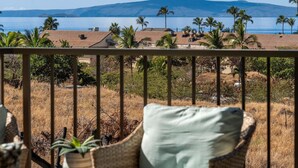 A balcony with a view of a coastal landscape, including a body of water, palm trees, and distant mountains. - Kihei Ali'i Kai D202 1 Bedroom Condo (Kihei)