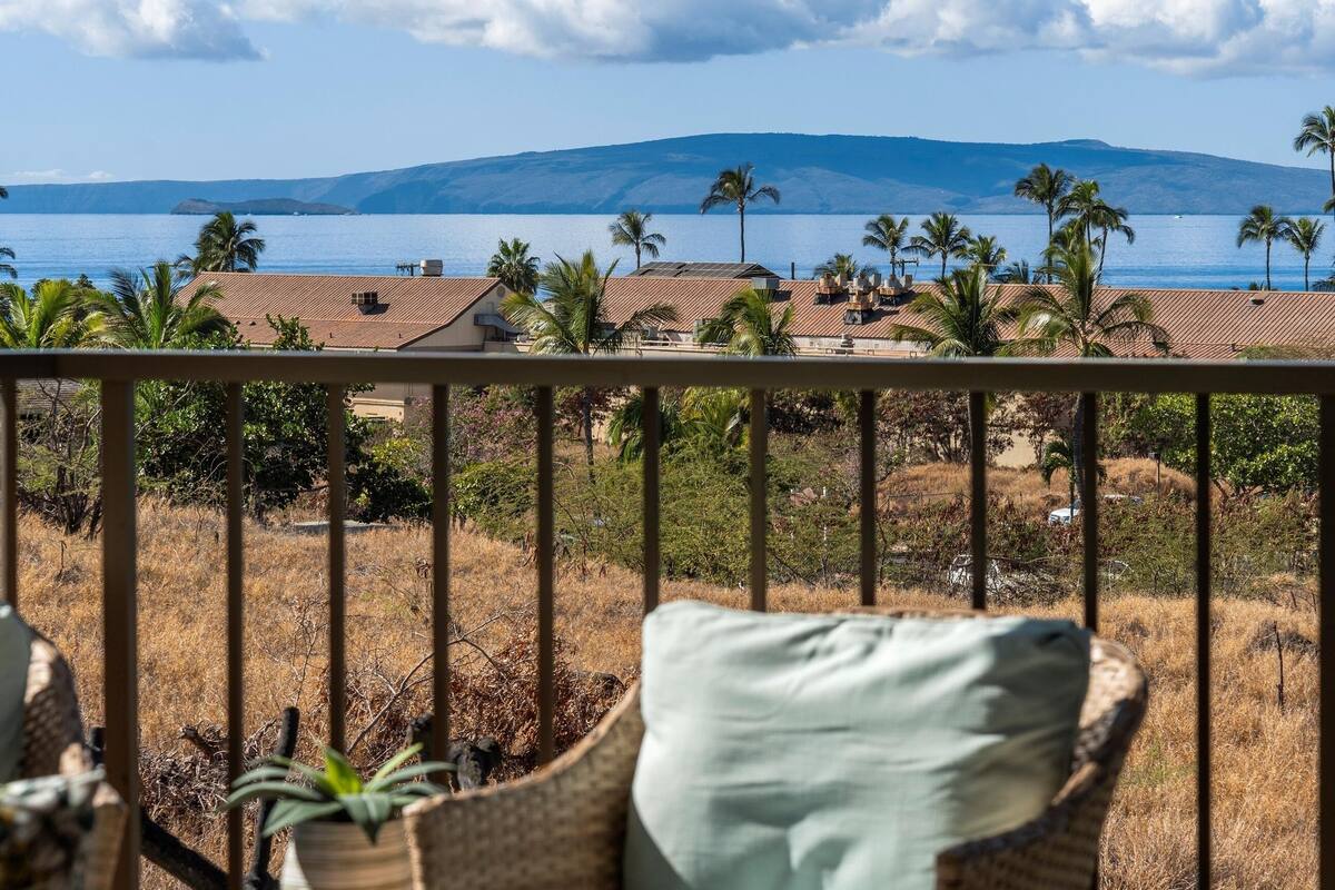 A balcony with a view of a coastal landscape, including a body of water, palm trees, and distant mountains.