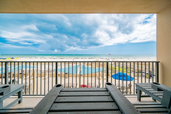A balcony with a view of a beach, pool, and umbrellas.