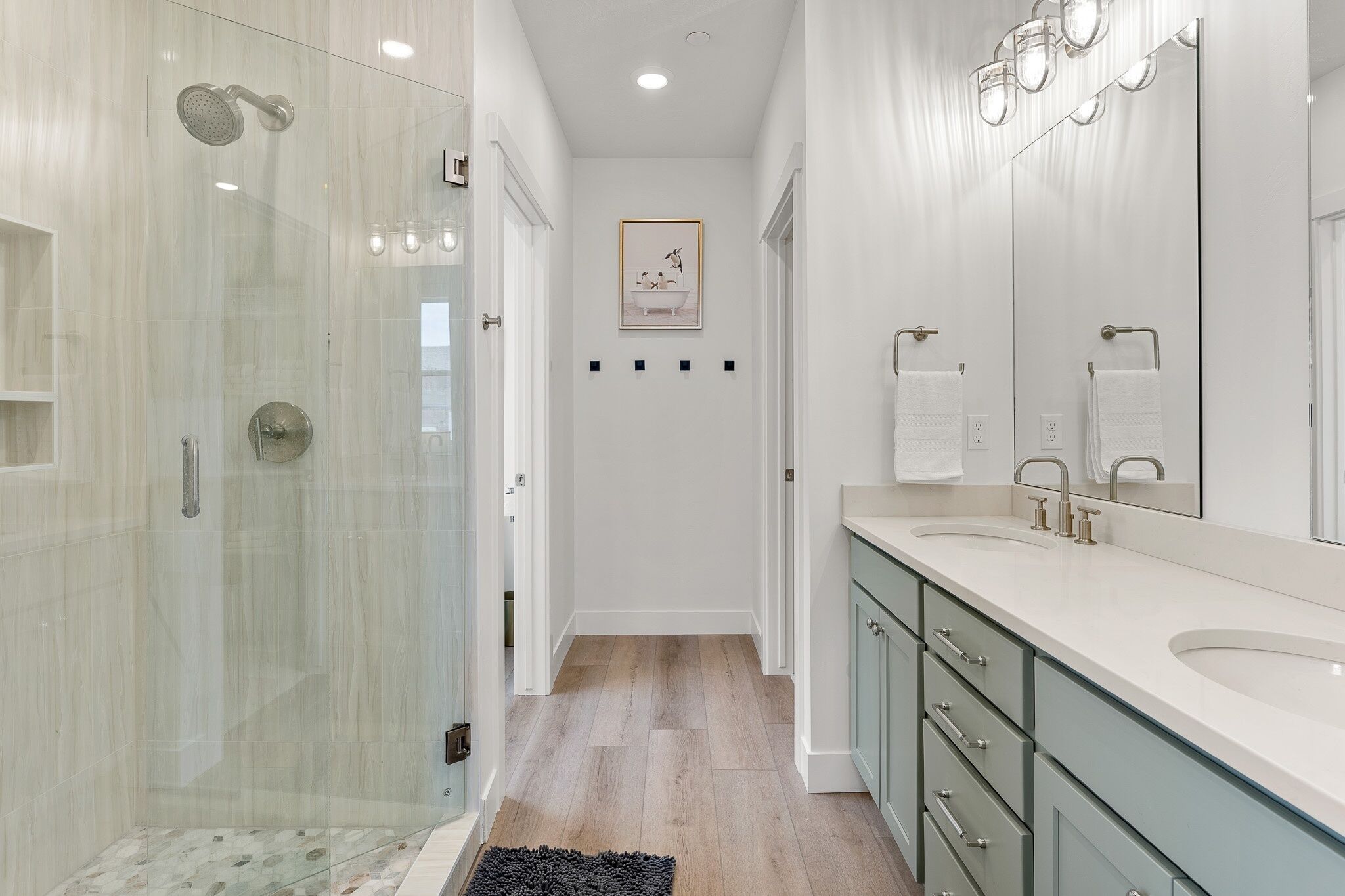 A modern bathroom with a glass-enclosed shower, a large vanity with a mirror, and a framed picture on the wall.