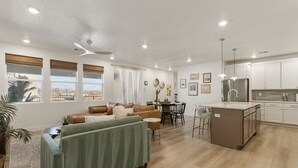 Un salon moderne avec un canapé vert, un divan en cuir marron et un coin repas comprenant une table et des chaises.