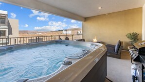 Un bain à remous avec vue sur un paysage désertique, un barbecue et un espace détente avec des coussins.