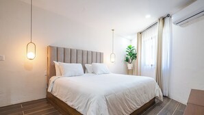 A modern bedroom with a large bed, wooden flooring, and a potted plant. - Charming Bungalow Cajititlan 2 Beds Pool (Tlajomulco de Zúñiga)