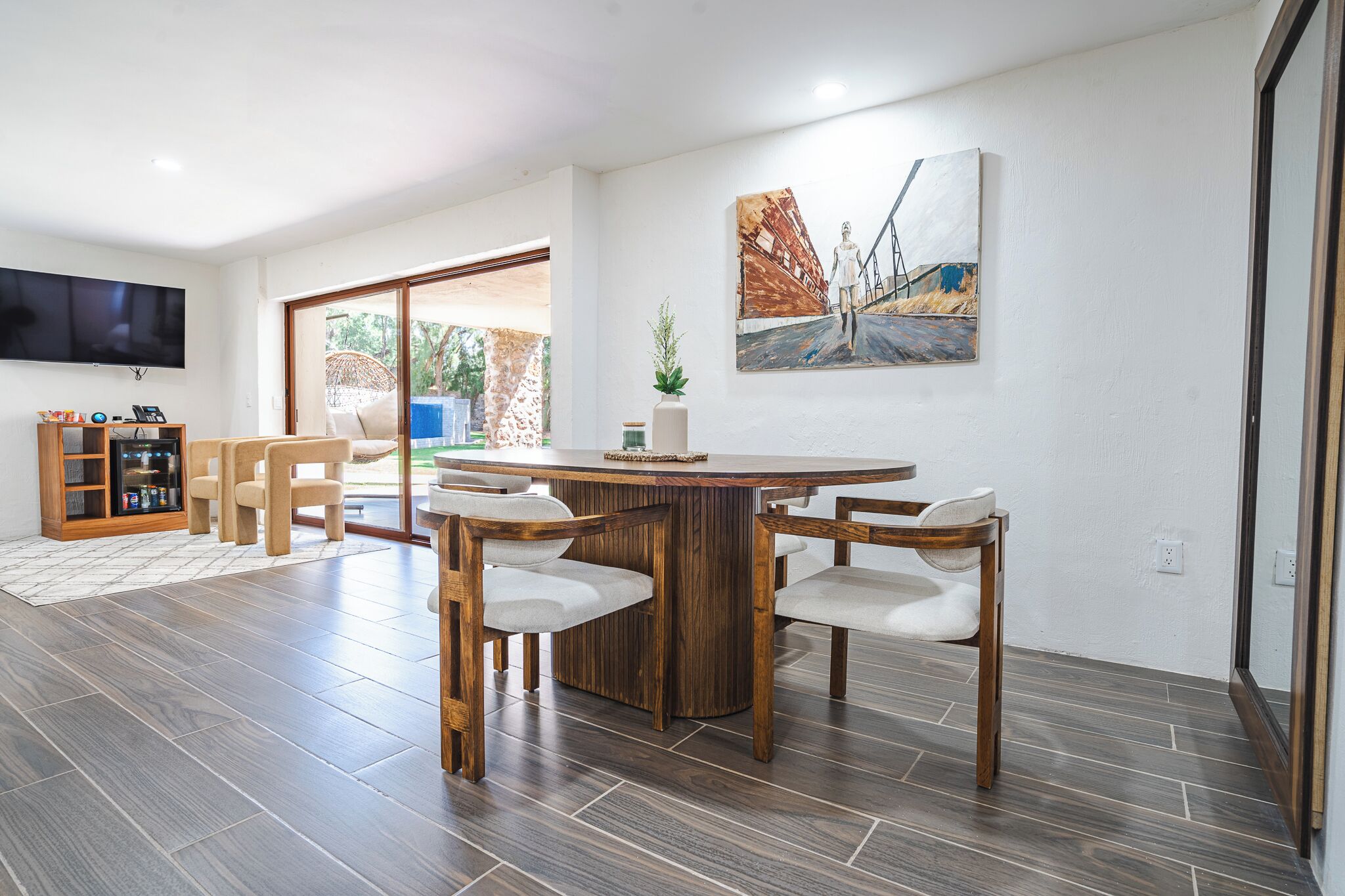 Un salón moderno con una mesa de comedor de madera, cuatro sillas, un televisor de pantalla plana y un amplio ventanal con vistas al exterior.