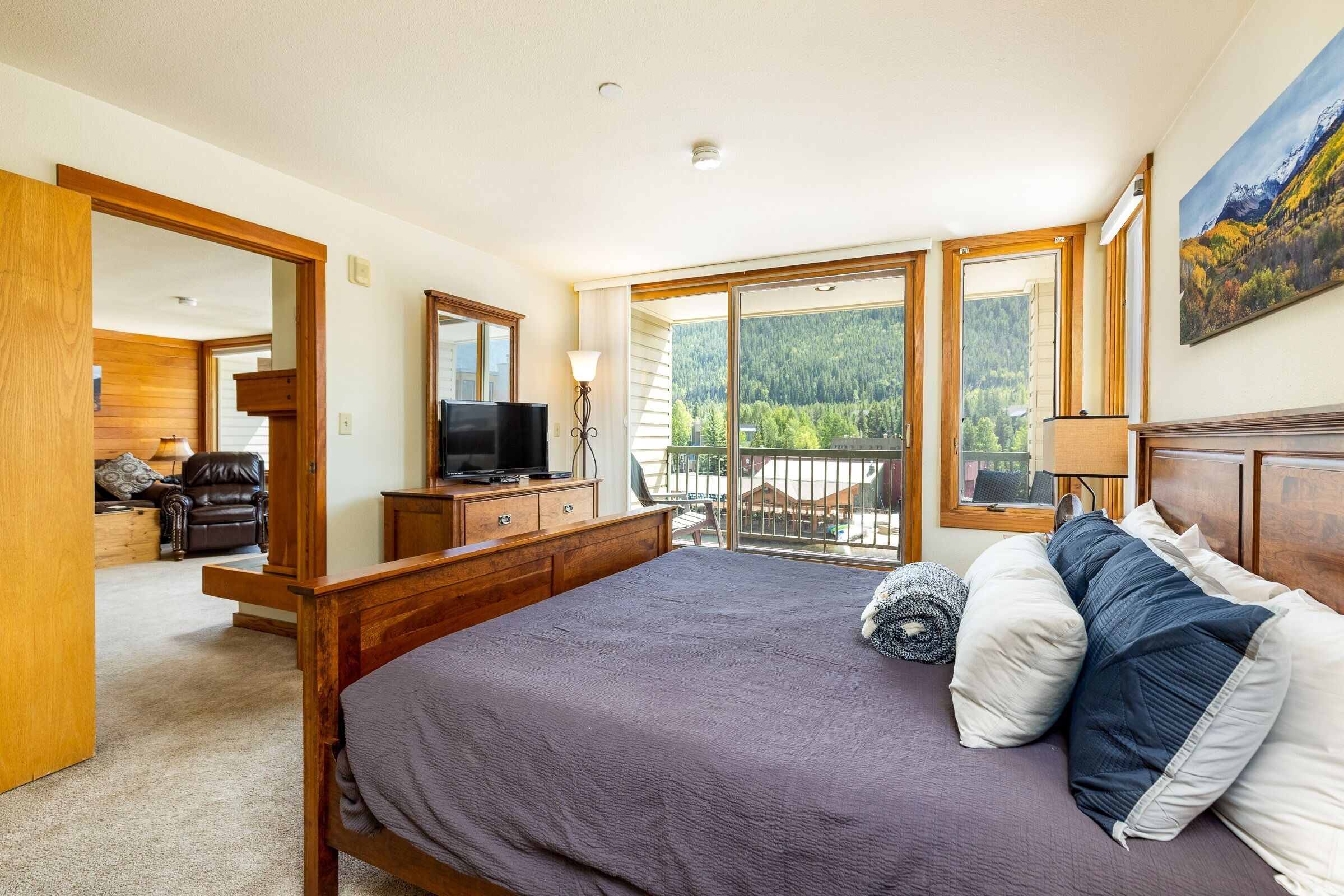 A bedroom with a large bed, a TV, a dresser, and a balcony with a mountain view.