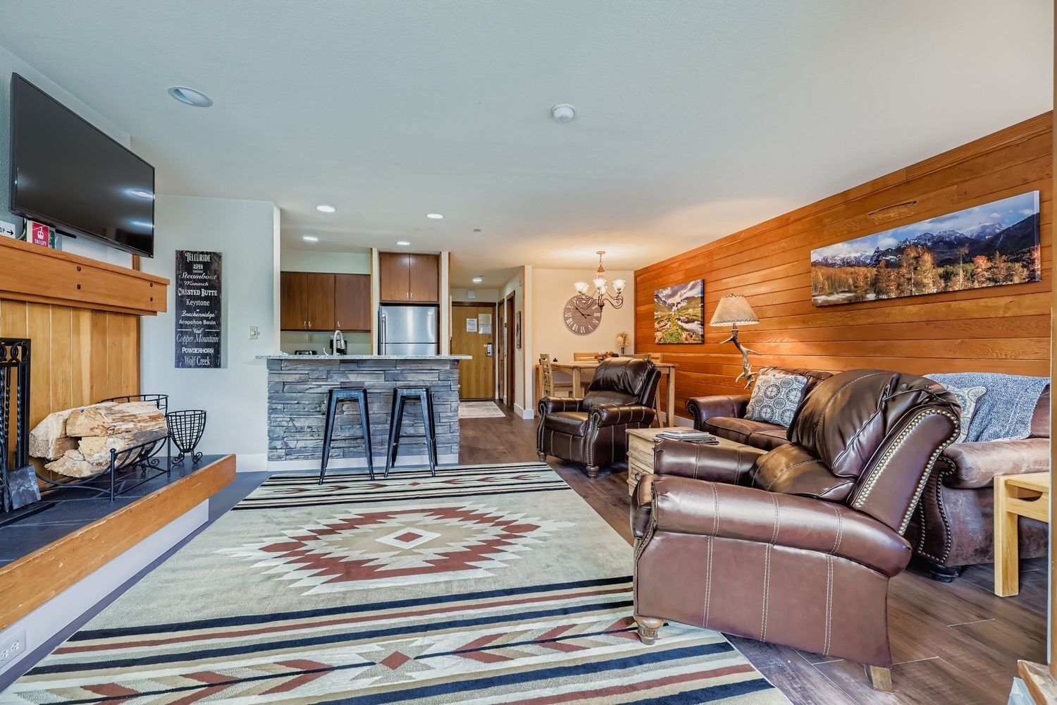 A modern living room with leather furniture, a stone island bar, and a wooden wall with a painting.