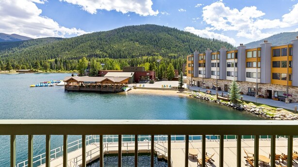 A lakeside hotel with a dock, outdoor seating, and a mountain backdrop. - 1483 Lakeside 1 Bedroom Condo (Keystone)