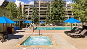 A pool area with lounge chairs and umbrellas, surrounded by tall trees and a multi-story building. - 1483 Lakeside 1 Bedroom Condo (Keystone)