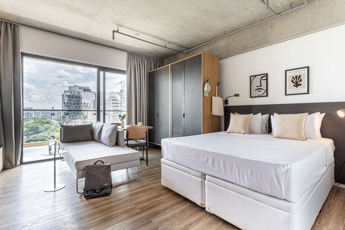 A modern hotel room with a large bed, a seating area, a wardrobe, and a city view.