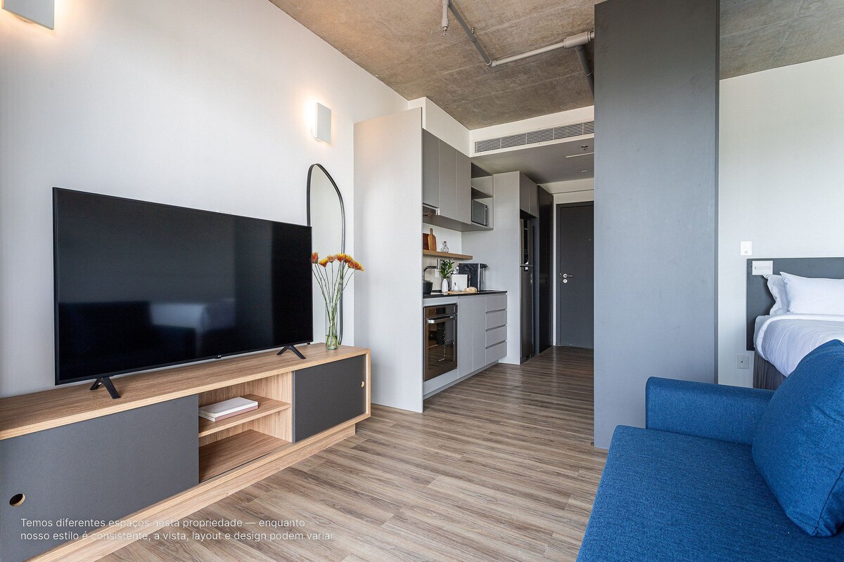 A modern living room with a flat-screen TV, a sofa, and a kitchen area in the background.