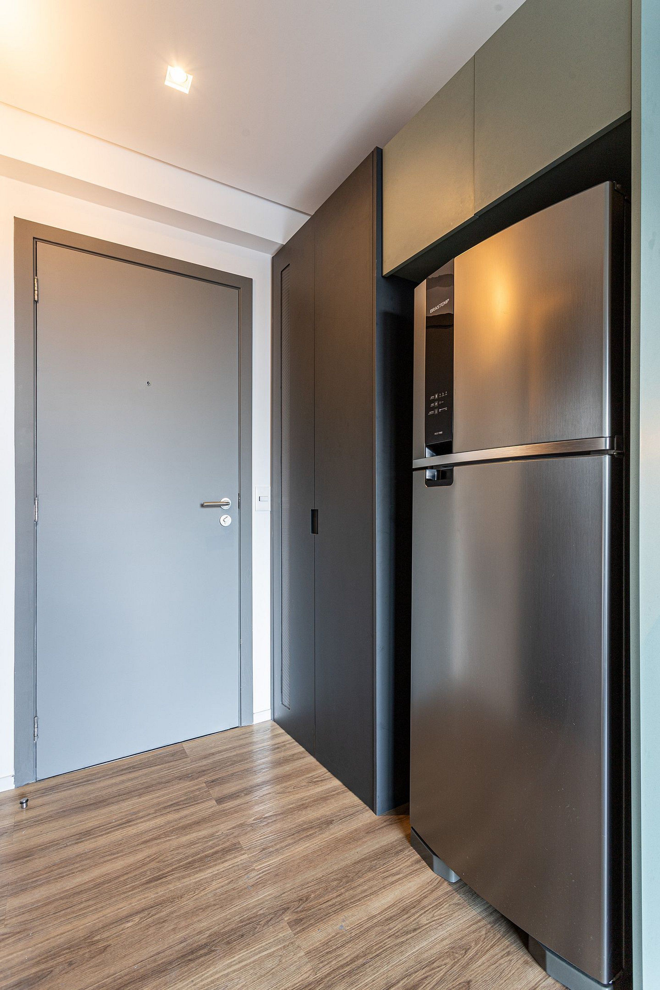 A modern kitchen with a stainless steel refrigerator, a wooden floor, and a closed door.