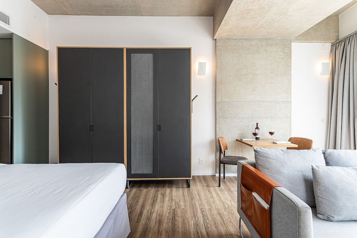 A hotel room with a bed, a wardrobe, a desk with a chair, and a sofa.