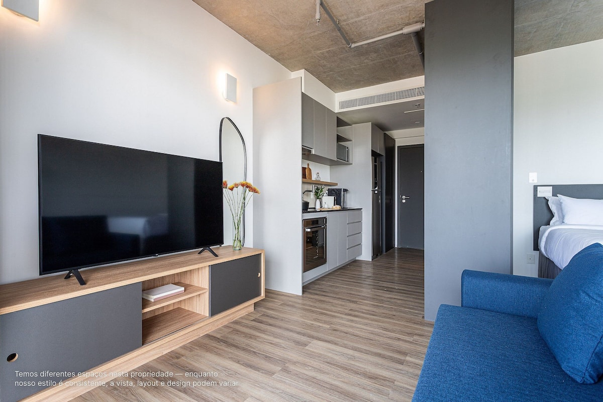 A modern living room with a flat-screen TV, a sofa, and a kitchen area in the background.