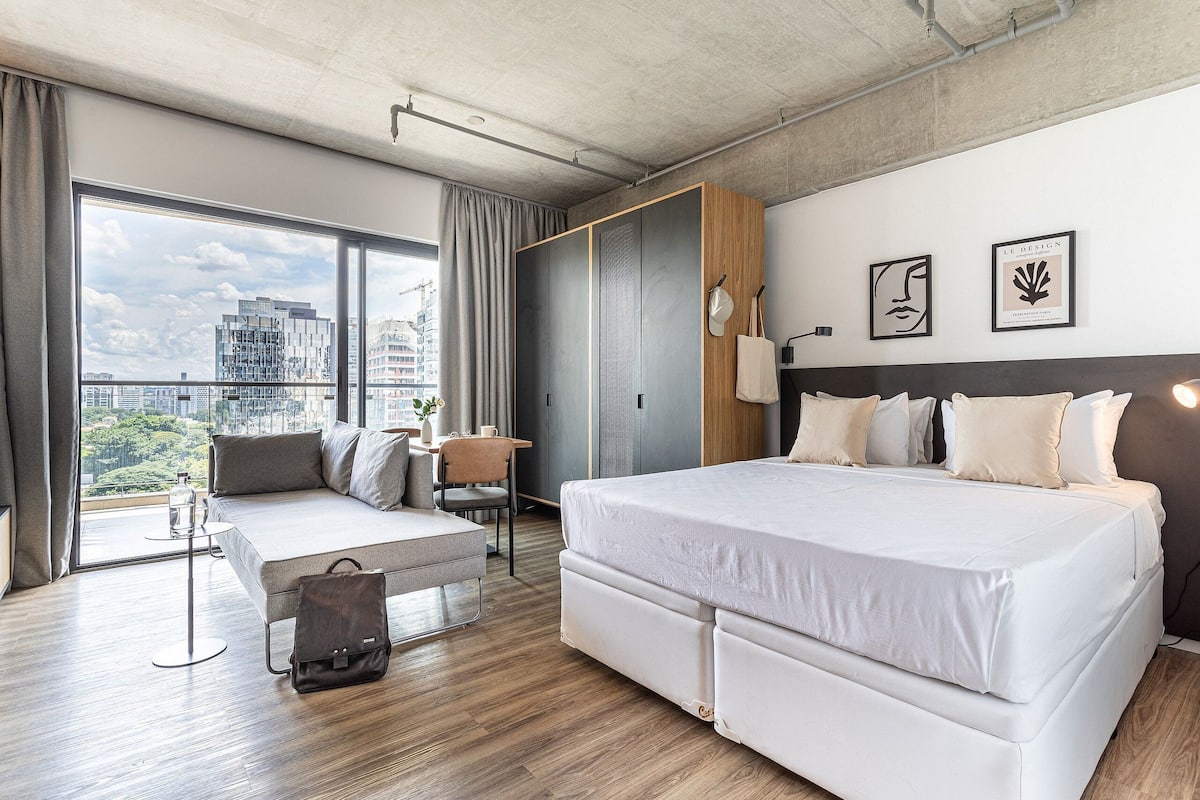 A modern hotel room with a large bed, a seating area, a wardrobe, and a city view.
