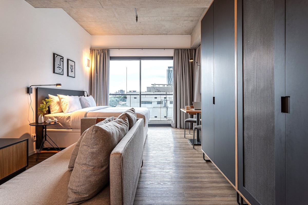 A modern hotel room with a bed, sofa, and a desk with a chair.