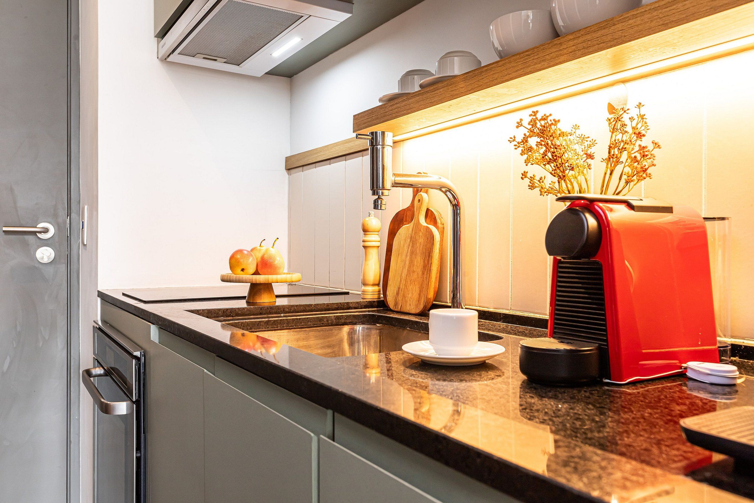 Una cocina moderna con un lavamanos de acero inoxidable, una cafetera roja y utensilios de madera.