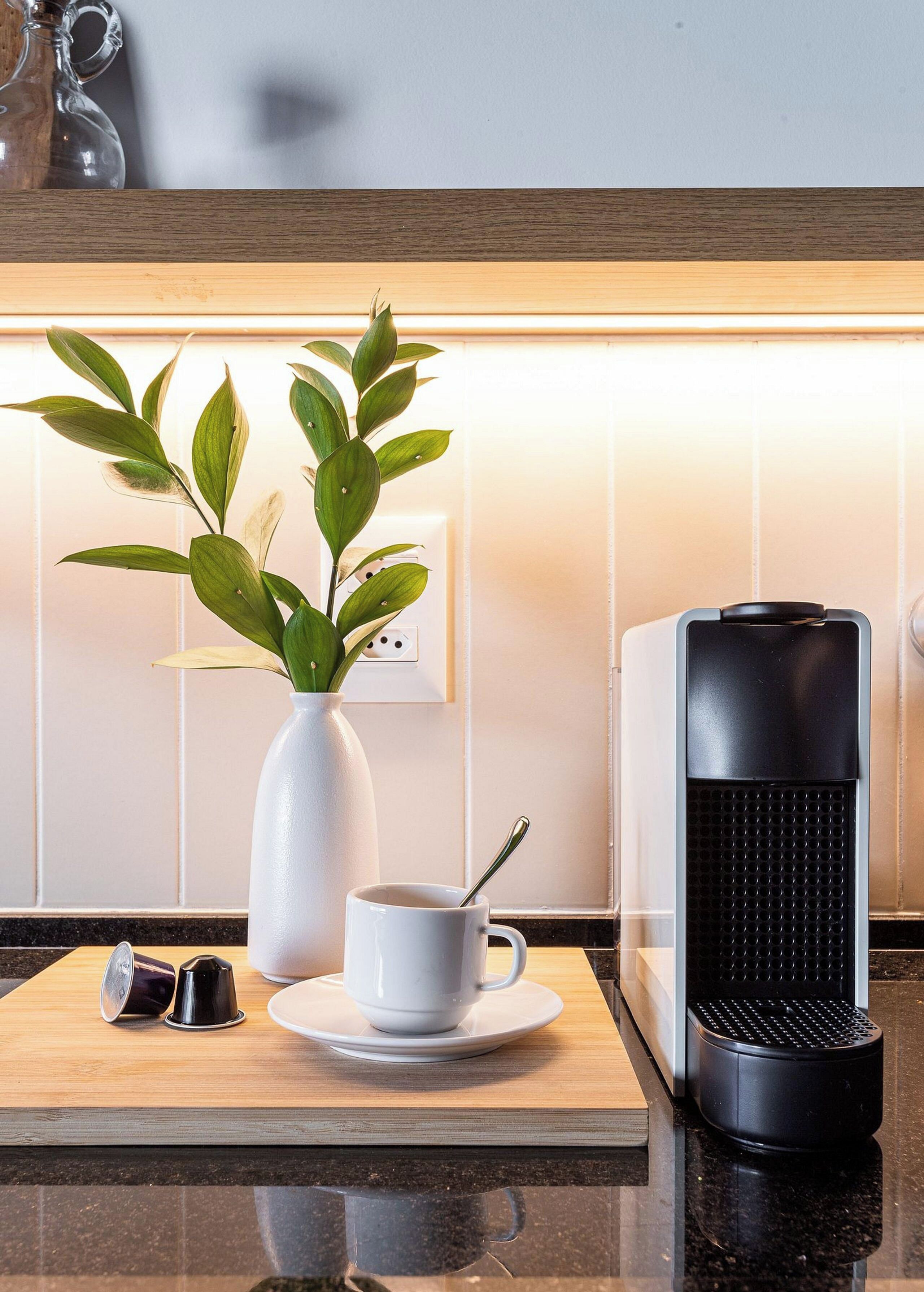 Un comptoir de cuisine avec une machine à café, une tasse blanche, une cuillère et une plante dans un vase blanc.