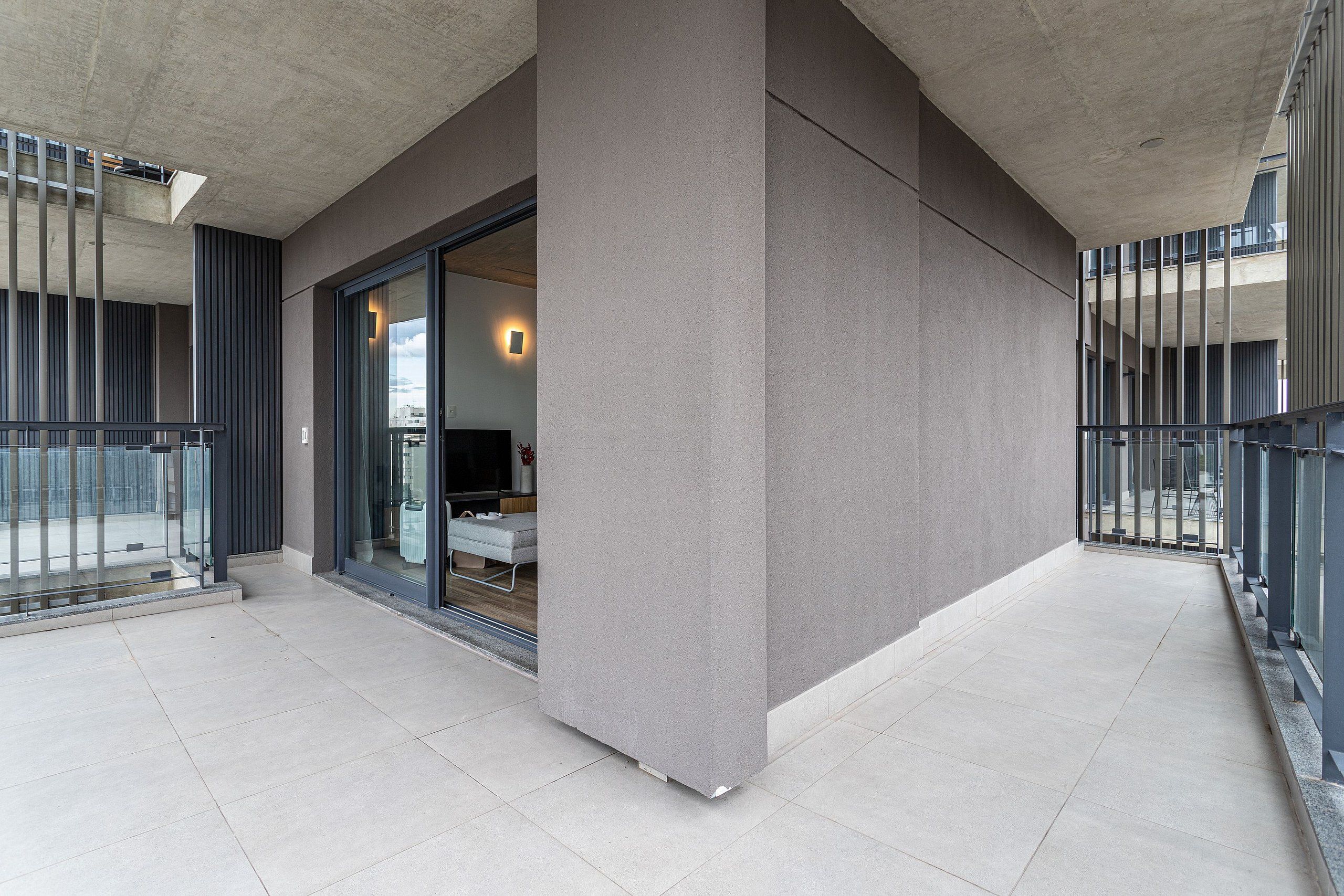 A modern building exterior with a balcony, large windows, and a visible door leading to an interior space.