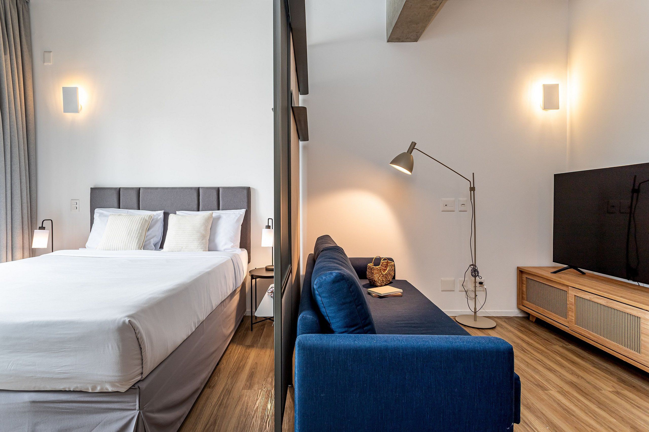 Una camera d'albergo moderna con un letto, un divano, una TV e una lampada.