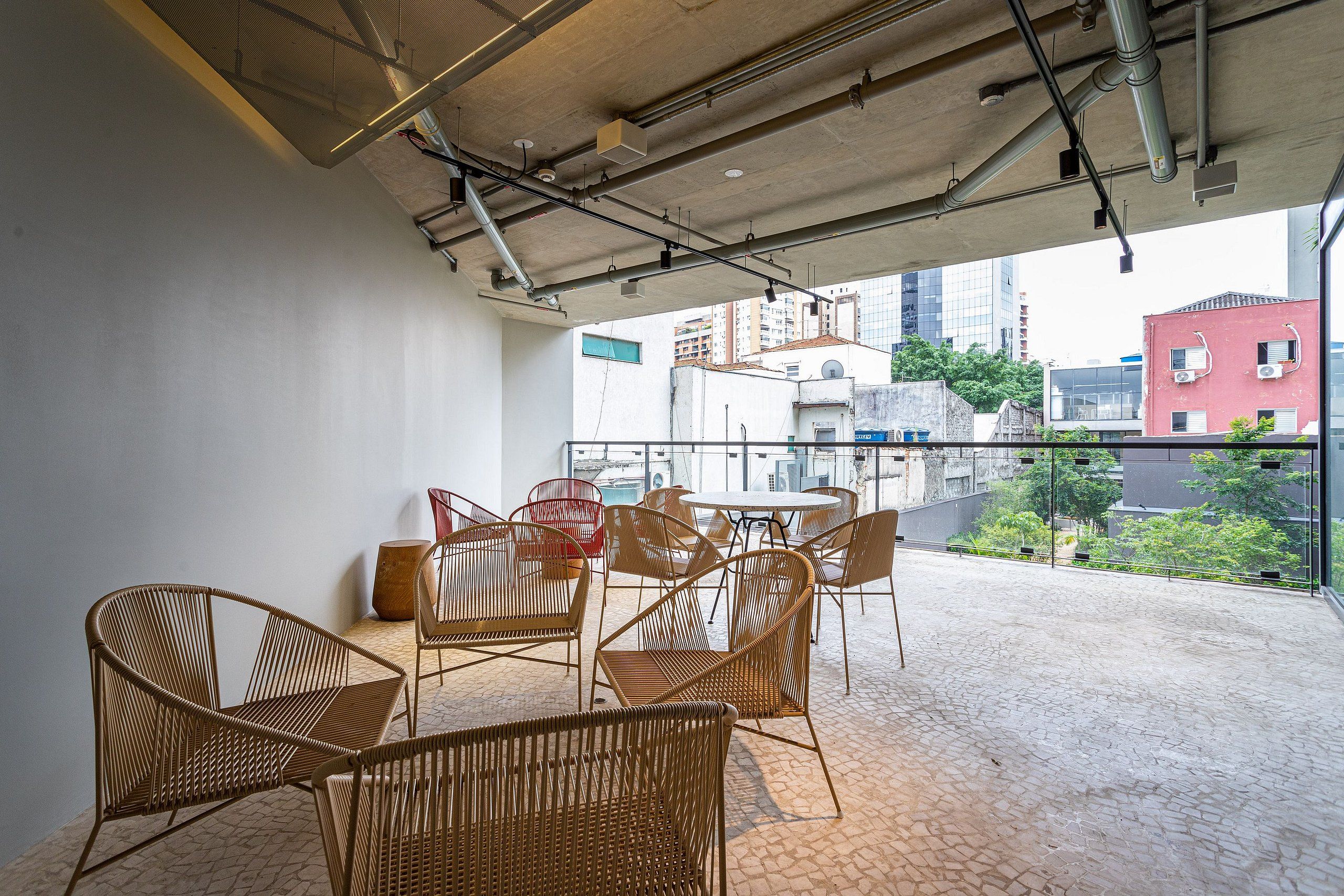 A balcony with wicker chairs and a table, overlooking a cityscape.