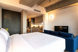 A hotel room with a bed, a seating area, a TV, and a kitchenette in the background. - Apartamentos com vista incrível para São Paulo ao lado da Rebouças e Faria Lima - Pinheiros (São Paulo)