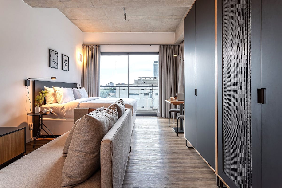 A modern hotel room with a bed, sofa, and a desk with a chair.