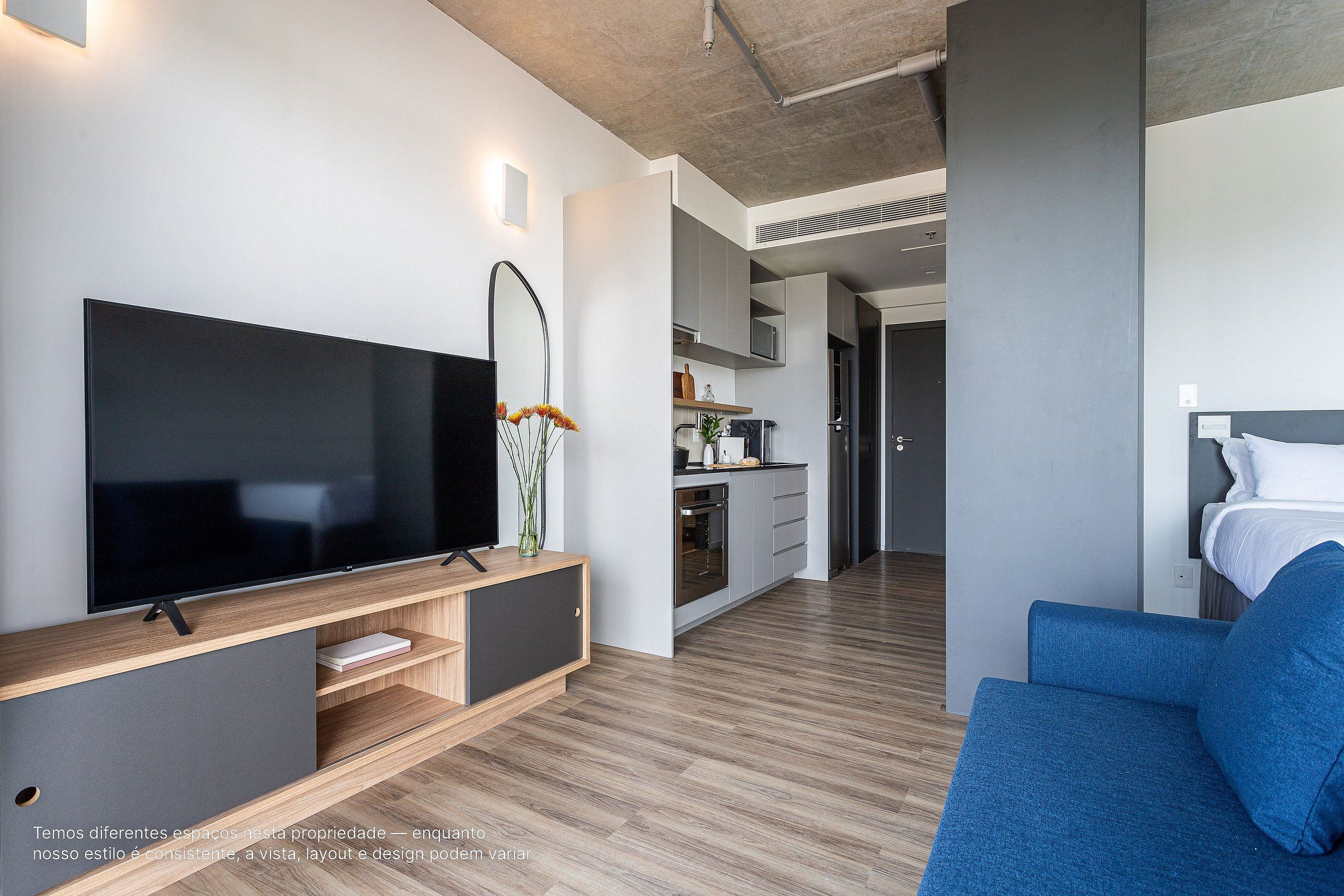 A modern living room with a flat-screen TV, a sofa, and a kitchen area in the background.