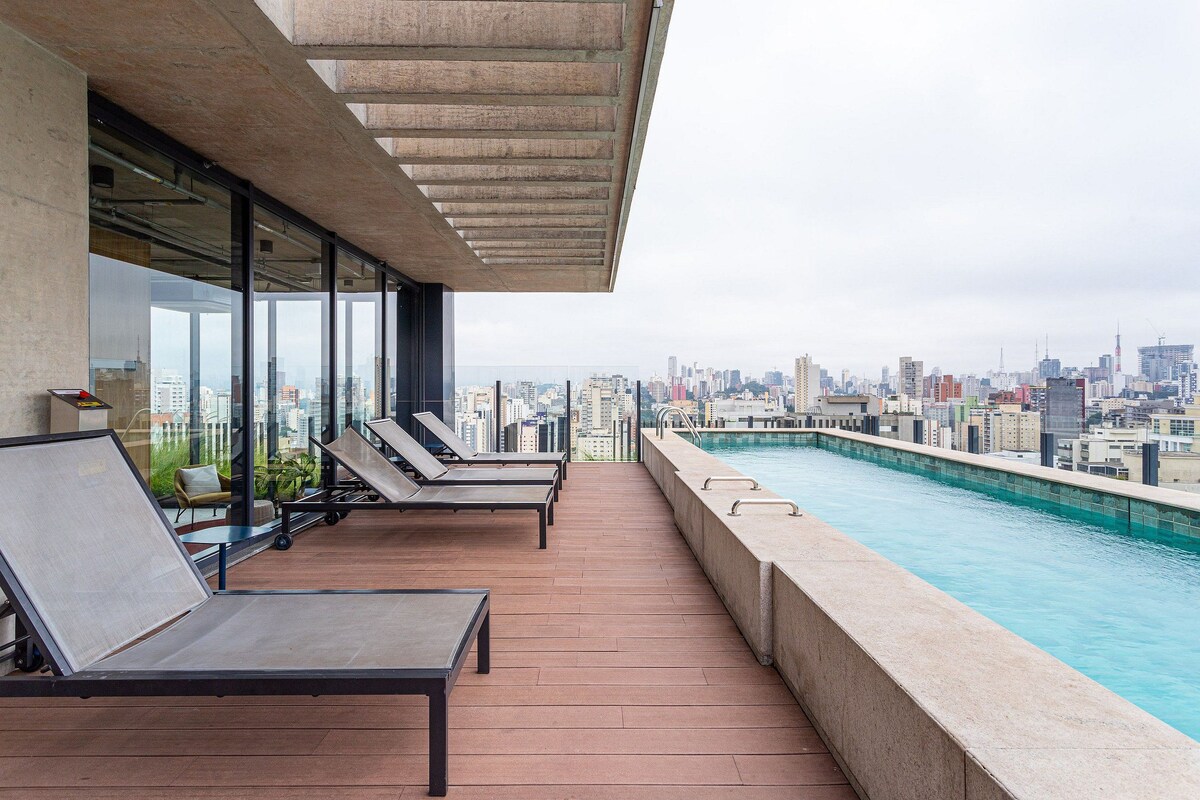 A rooftop pool area with lounge chairs, a view of the city skyline, and a pool with clear water.