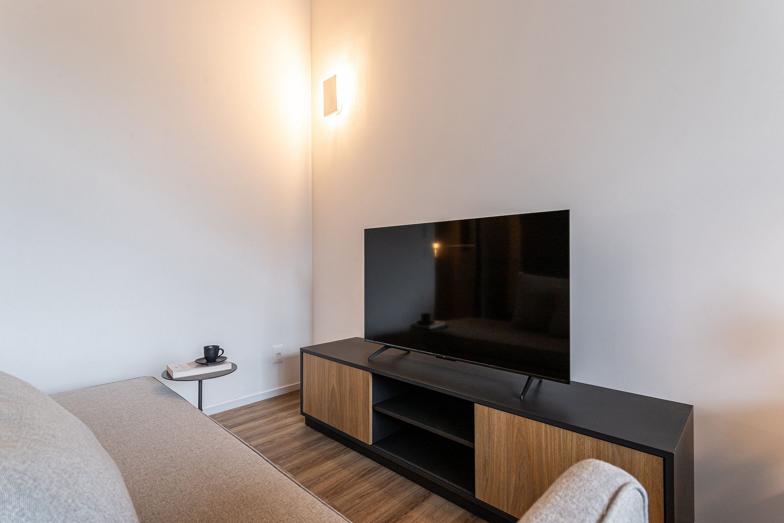 Ein modernes Wohnzimmer mit einem Flachbildfernseher, einem kleinen Beistelltisch mit einer Tasse und einem Sofa.