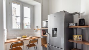 A compact kitchen with a stainless steel refrigerator, a microwave, and a small dining area with two chairs. - Le Milady - Charmant appartement au cœur de Rennes (Rennes)