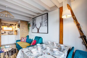 A cozy dining area with a table set for four, a blue sofa, and a ski-themed wall decoration. - Les Alysses - Maison pour 5 avec garage (Font-Romeu)