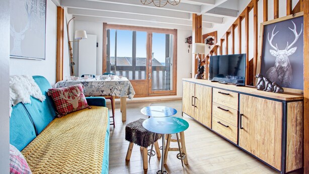 En hyggelig stue med sofa, spisebord og et køkkenområde med træskabe og et fjernsyn.