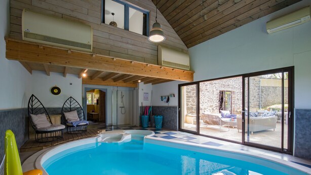 Ein Innenpool mit Schachbrettmuster-Boden, Holzbalken an der Decke und Blick auf eine Außenpatio mit Möbeln.