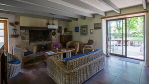 Ein gemütliches Wohnzimmer mit Korbmöbeln, einem Kamin und einer großen Glasschiebetür, die auf eine Terrasse im Freien führt.