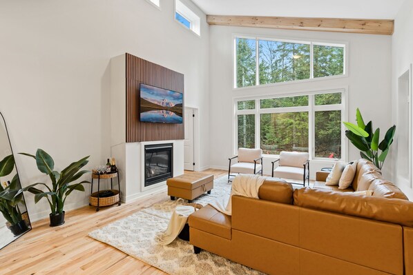 Ein modernes Wohnzimmer mit Kamin, Ledersofa und großen Fenstern mit Blick ins Freie.
