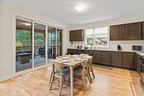 Eine moderne Küche mit Holzschränken, ein Essbereich mit Tisch für vier Personen und eine Glastür, die auf eine Terrasse im Freien führt.