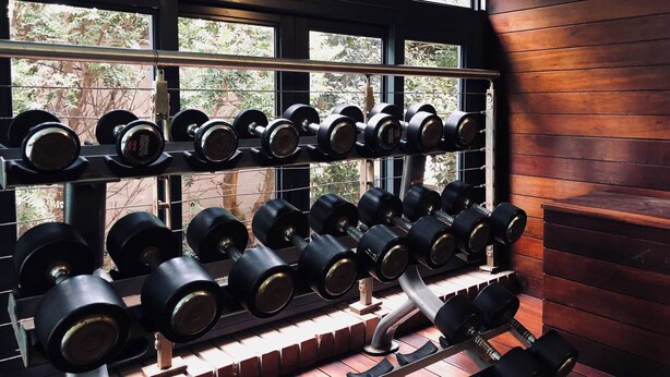 Une salle de sport avec plusieurs rangées d’haltères et un mur en briques.