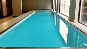 Une piscine intérieure à l’eau d’un bleu limpide, entourée de murs et de fenêtres.