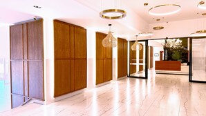 Un hall d’hôtel moderne avec des lambris en bois, un sol en marbre et des luminaires contemporains.