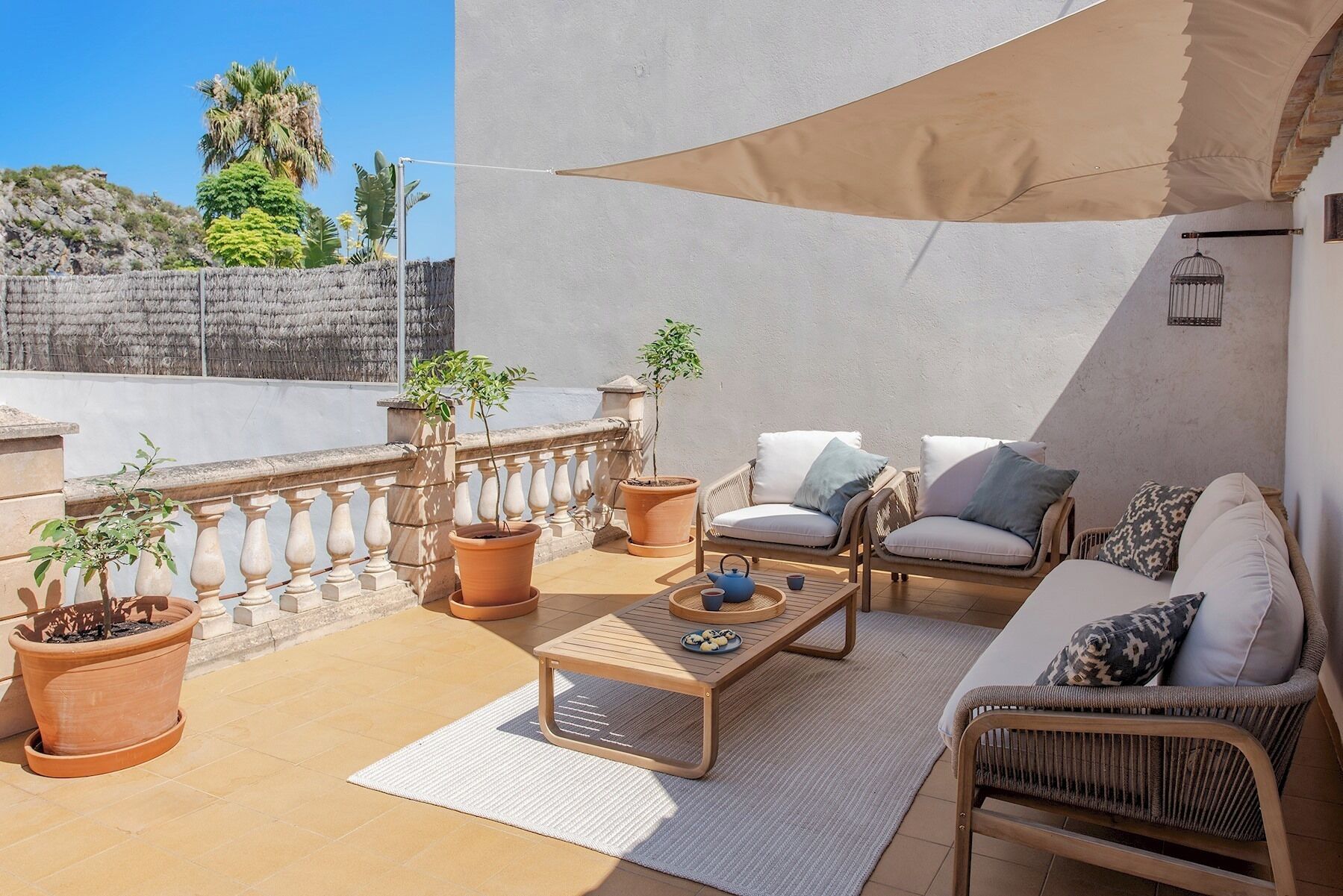 A sunlit outdoor patio with wicker furniture, terracotta planters, and a view of the surrounding landscape.