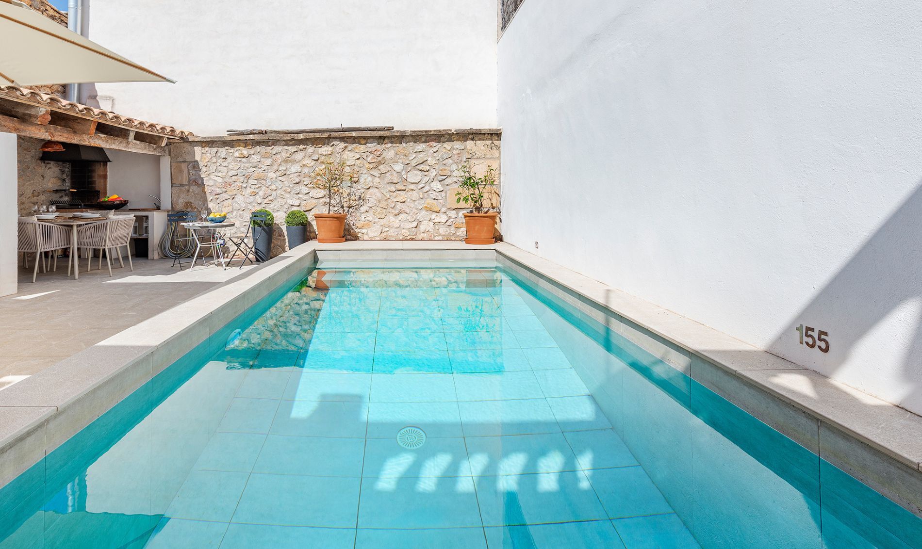 A swimming pool with a stone wall and a patio area with a table and chairs.