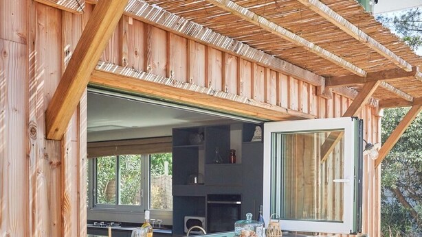 A wooden deck with a bar area, bar stools, and a view of the kitchen.