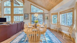 A cozy living room with a wooden ceiling, large windows, a sofa, a dining table with chairs, and a TV. - Hansel by Avantstay Pool Table, 5mins to Skiing (Truckee)