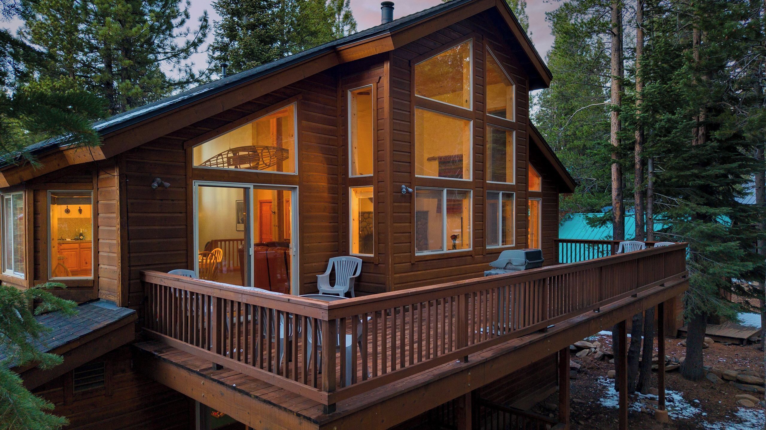 A wooden cabin with a deck, large windows, and a stone fireplace.