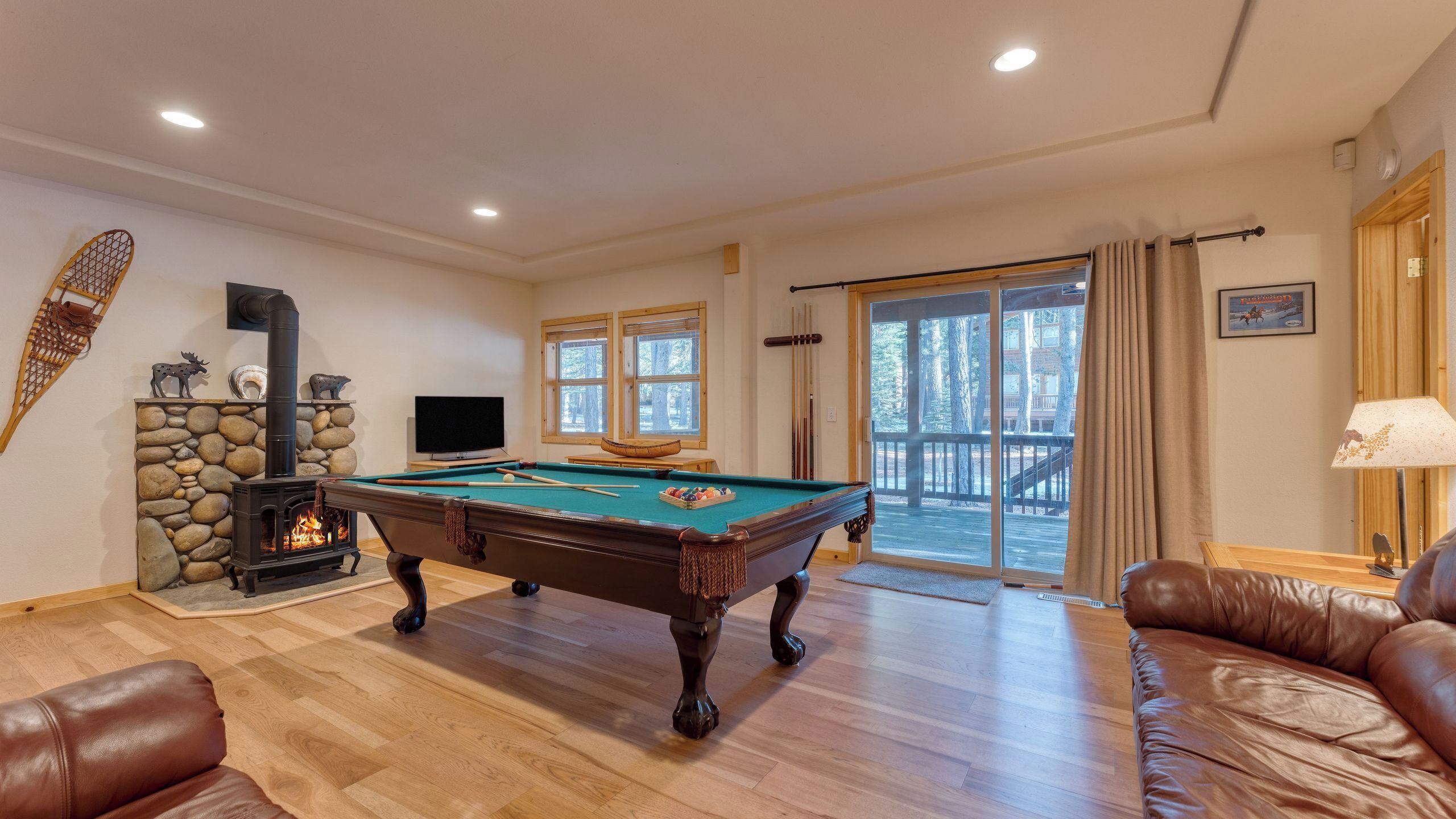 A cozy living room with a pool table, a fireplace, and a large window overlooking a deck.