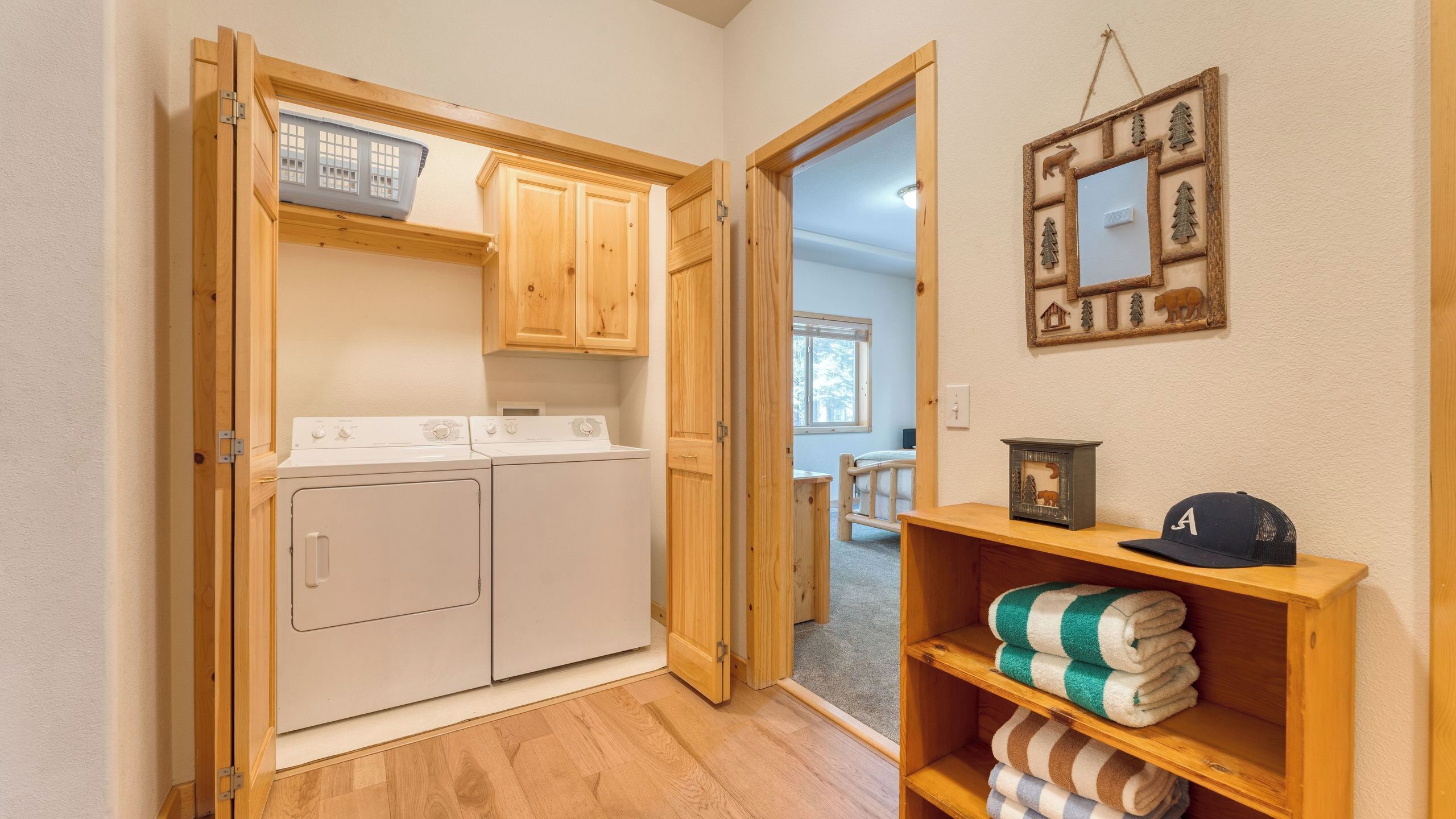 A laundry room with two washing machines, wooden cabinets, and a shelf with folded towels.