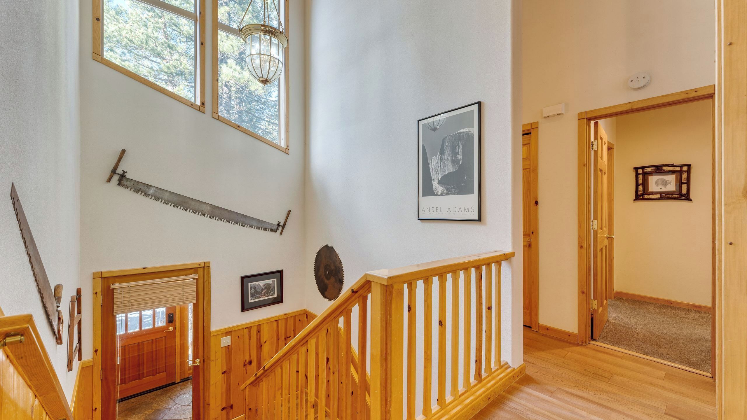 Un escalier avec des rampes en bois, un tableau encadré au mur et une fenêtre donnant sur des arbres.