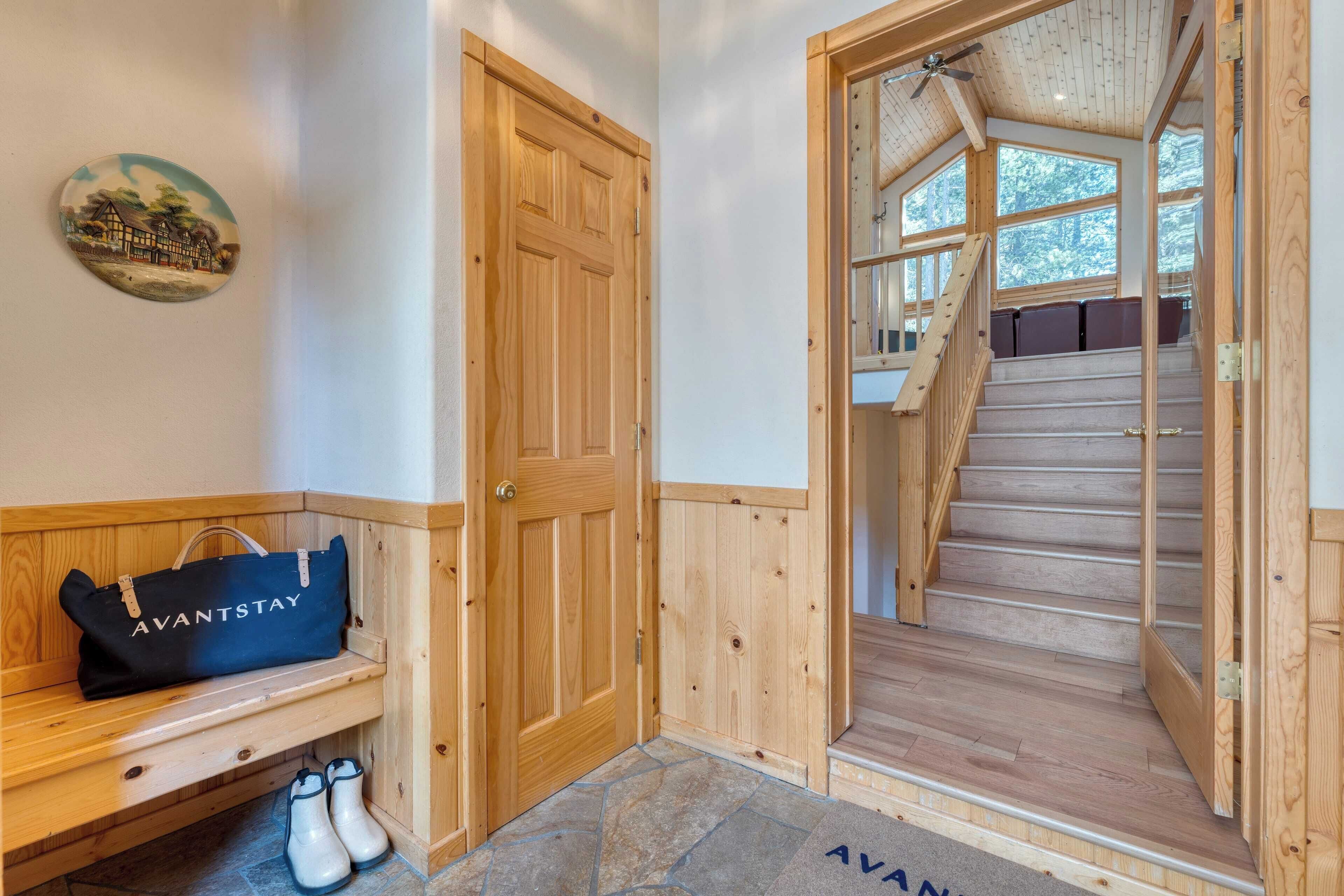 A wooden interior with a bench, a door, and a staircase leading to a room with a view of trees.