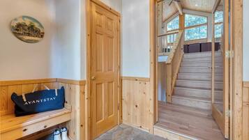 A wooden interior with a bench, a door, and a staircase leading to a room with a view of trees.
