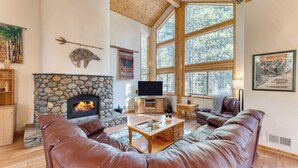 A cozy living room with a stone fireplace, leather sofas, and large windows offering a view of the forest. - Hansel by Avantstay Pool Table, 5mins to Skiing (Truckee)
